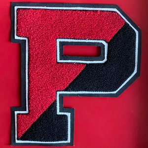 May include: A red and black felt letter P with white stitching around the edges. The letter is a patch or applique.