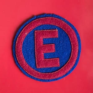 May include: A red felt letter E with a blue felt circle around it. The letter is sewn onto the circle.