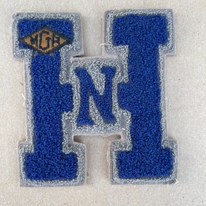 May include: A blue felt letter H with a gray outline and a small brown diamond-shaped patch with the letters "MGH" inside. The letter H is a vintage style felt patch.