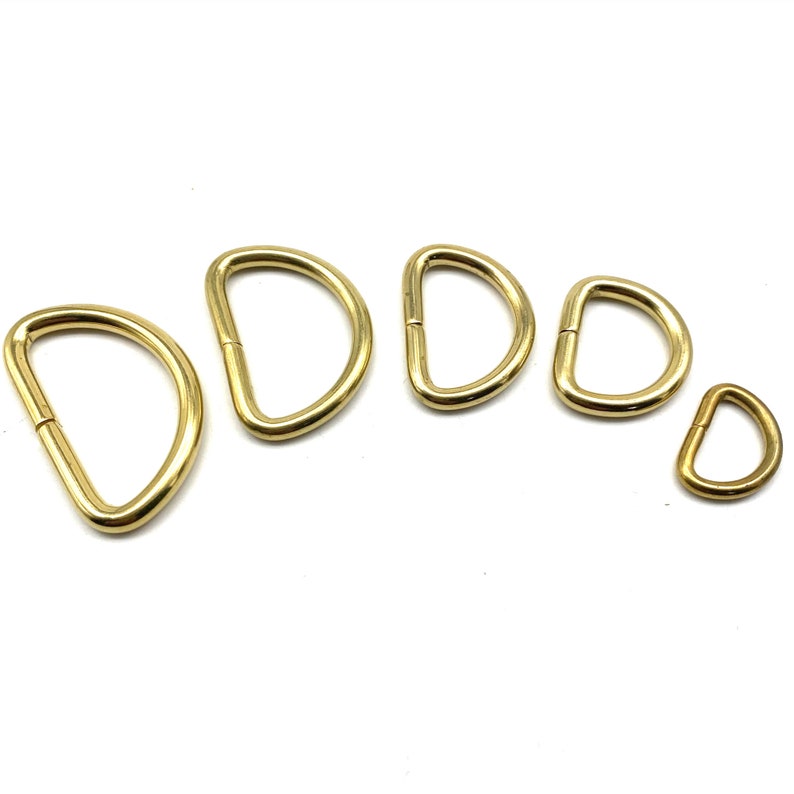 May include: Five gold-toned metal D-rings of varying sizes. The rings are arranged in a semi-circle, with the smallest ring at the bottom right.