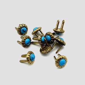 May include: A group of 10 turquoise and brass decorative tacks with a flower design. The tacks have two prongs on the back for attaching to fabric.