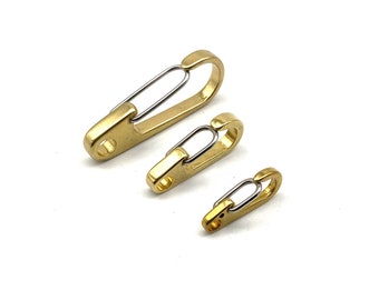 Puede incluir: Tres mosquetones de resorte de latón de diferentes tamaños. Cada mosquetón tiene un cuerpo dorado y una puerta con resorte plateada. Los mosquetones están dispuestos diagonalmente sobre un fondo blanco, mostrando su diseño.