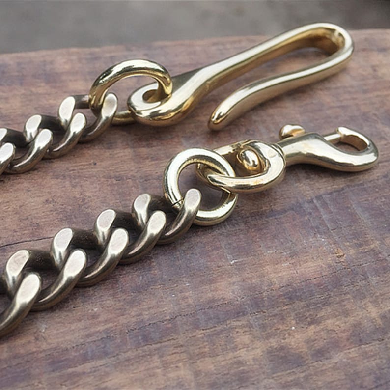 May include: A brass key chain with a thick, curb chain and two different styles of clasps. One clasp is a simple hook and the other is a swivel hook.