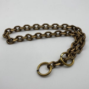 Op de afbeelding: Een gouden ketting met een ring aan het einde. De ketting is gemaakt van in elkaar grijpende metalen schakels.