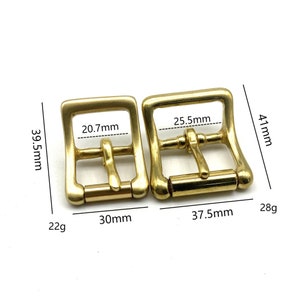 Może przedstawiać: Dwie złote metalowe klamry do paska, jedna o wymiarach 30 mm x 39,5 mm i wadze 22 g, druga o wymiarach 37,5 mm x 41 mm i wadze 28 g.