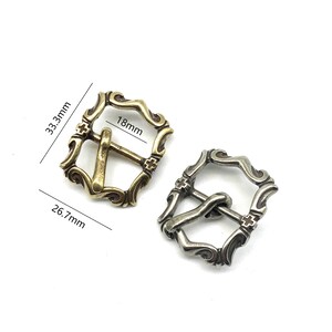 May include: Two ornate metal belt buckles, one gold and one silver, with a cross design and a measurement of 18mm. The buckles are 3.3 cm wide and 2.6 cm tall.