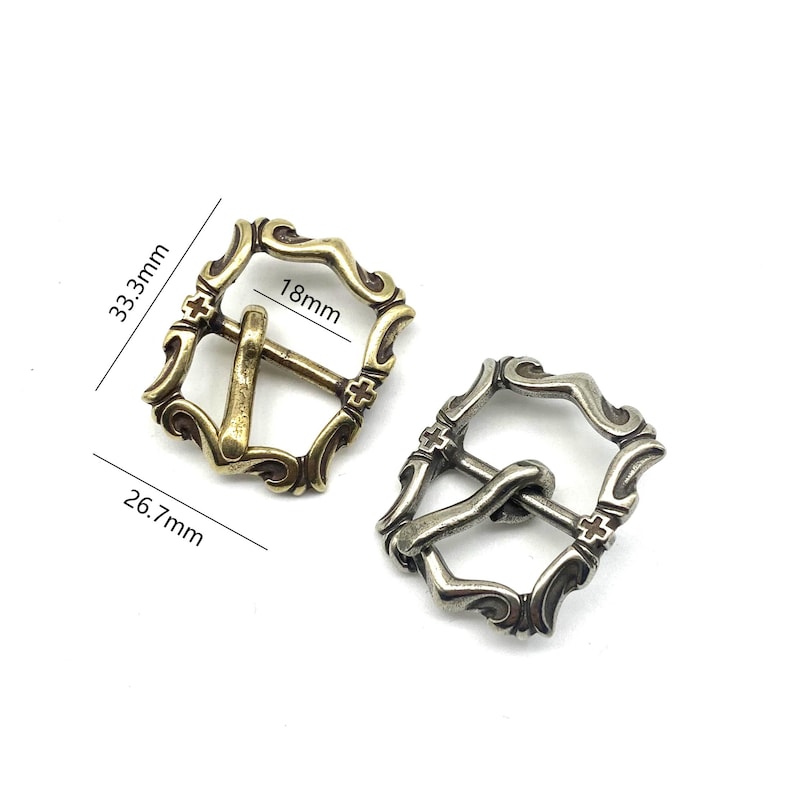 May include: Two ornate metal belt buckles, one gold and one silver, with a cross design and a measurement of 18mm. The buckles are 3.3 cm wide and 2.6 cm tall.