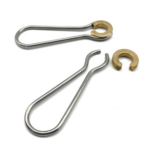 Puede incluir: Dos anillos de metal plateado con un anillo de metal dorado unido a cada uno. Los anillos están abiertos por un lado y tienen una forma redondeada.