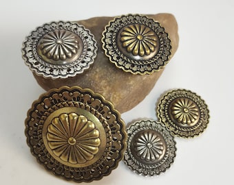 May include: Four decorative metal embellishments with a floral design. The embellishments are in two sizes and two colours: silver and gold.