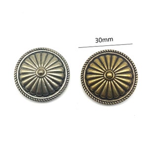 Pode incluir: Dois botões decorativos redondos de metal com um design de raios de sol. Os botões têm um diâmetro de 30 mm e uma borda de corda. Um botão é prateado e o outro é dourado.