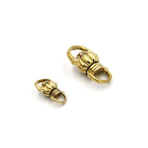 Könnte beinhalten: Zwei goldfarbene Metallverschlüsse mit einem dekorativen Design. Der größere Verschluss ist etwa 2,5 cm lang und der kleinere etwa 1,25 cm lang.