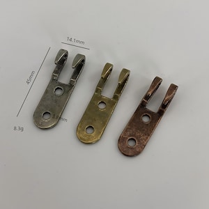 Puede incluir: Tres soportes metálicos en forma de U en tonos plateado, dorado y cobrizo. Cada soporte tiene dos clavijas y un orificio para el montaje. Los soportes miden 4,5 cm de largo, 1,4 cm de ancho, 0,4 cm de grosor y pesan 8,3 g.