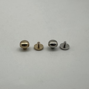 Op de afbeelding: Vier metalen klinknagels op een rij, elk met een afgeronde kop en een schroefdraad. Twee zijn goudkleurig en twee zilverkleurig. De klinknagels zijn ontworpen om materialen te verbinden.