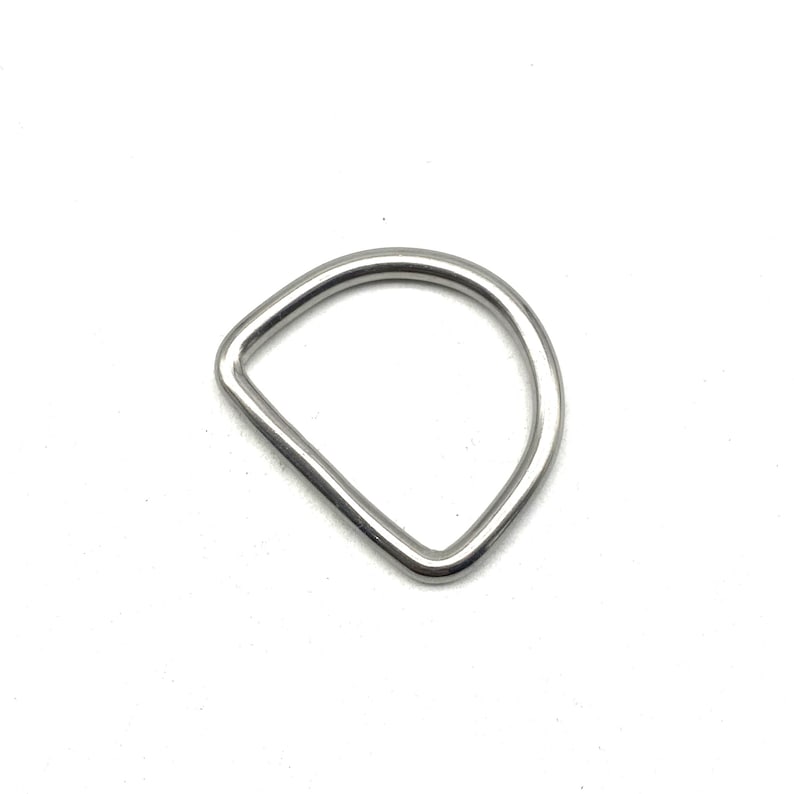 Op de afbeelding: Een zilveren metalen D-ring. Dit type ring wordt vaak gebruikt om banden, riemen of andere accessoires aan te bevestigen.