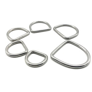 Può includere: Un set di sei anelli a D in metallo argentato di diverse dimensioni. Gli anelli sono disposti in cerchio su uno sfondo bianco.