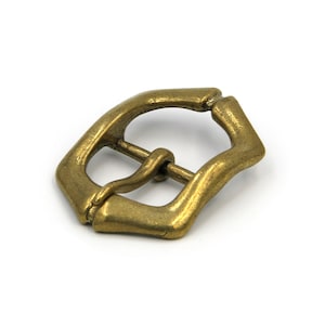 May include: A gold-toned metal buckle with a simple, slightly curved design. The buckle is designed to be used with a strap or belt.