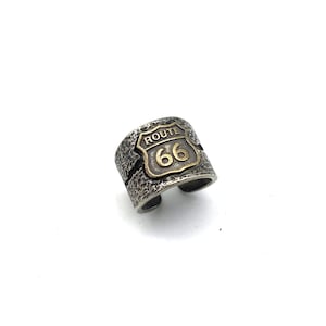 May include: A silver ring with a textured finish featuring a gold Route 66 sign.