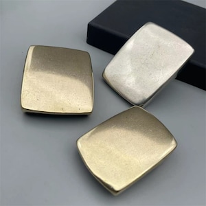 Può includere: Tre fibbie per cintura in metallo in diverse finiture: oro, ottone e argento. Le fibbie sono rettangolari e hanno una superficie liscia e lucida.