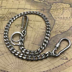 May include: A silver-colored wallet chain with a curb chain design. The chain features a hook on one end, a key ring, and a carabiner clip on the other. The chain is displayed on a vintage map background.