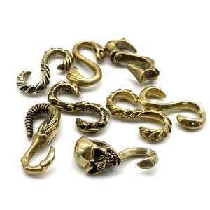May include: A collection of nine brass keychains with different designs, including a skull, a snake, and a swirl pattern.