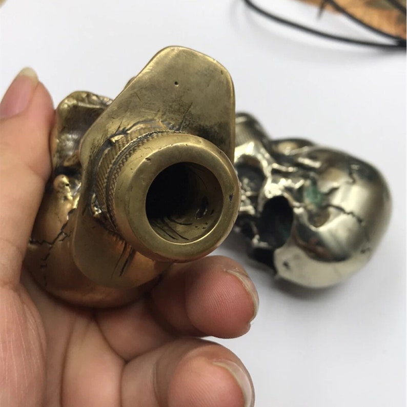 May include: Close-up of a brass skull cane handle with a threaded opening. The handle is detailed with a skull design and has a silver finish on the skull.