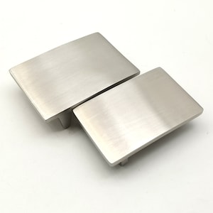 Puede incluir: Dos tiradores de armario de níquel cepillado, uno ligeramente más grande que el otro, con forma rectangular y bordes redondeados.