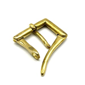 May include: A gold-toned metal buckle with a square frame and a curved, hinged lever. The buckle is designed for a belt or strap.
