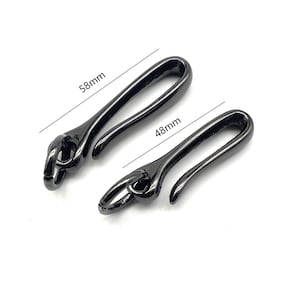 Könnte beinhalten: Zwei schwarze Metallhaken mit einer abgerundeten Schlaufe an einem Ende. Der größere Haken ist 58 mm lang und der kleinere Haken ist 48 mm lang.