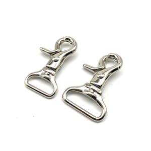May include: Two silver metal swivel snap hooks with a rectangular loop. The hooks are commonly used for attaching leashes, straps, or other accessories.