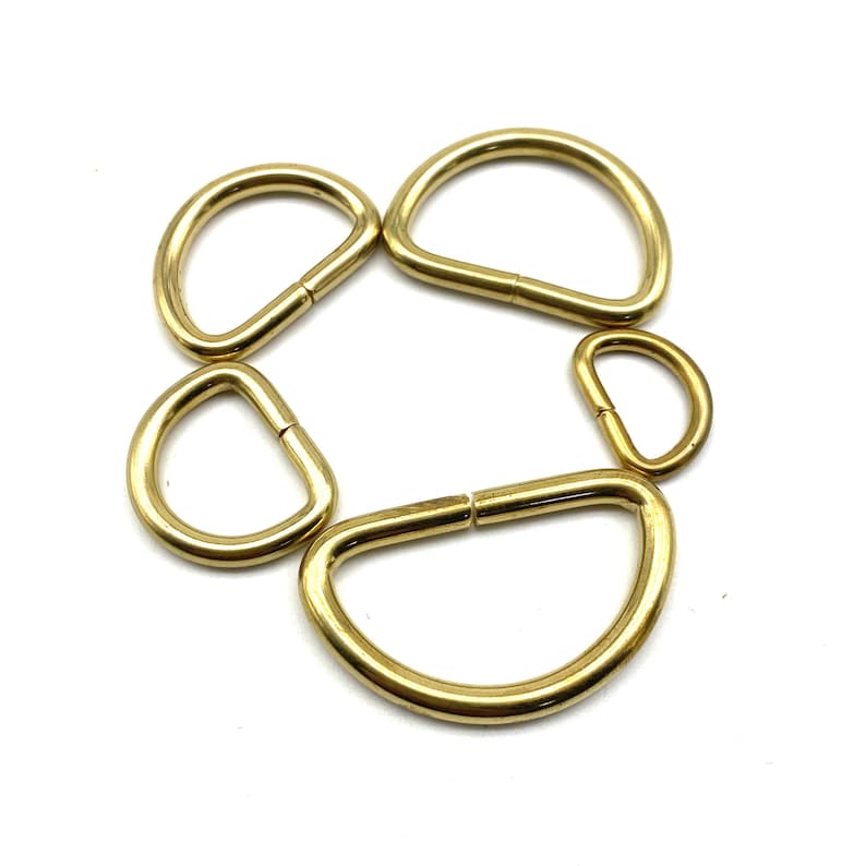 May include: Five gold-toned metal D-rings of varying sizes. The rings are arranged in a circle.