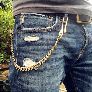 May include: A gold chain with a hook attached to a pair of blue jeans. The chain is worn as a belt loop accessory.