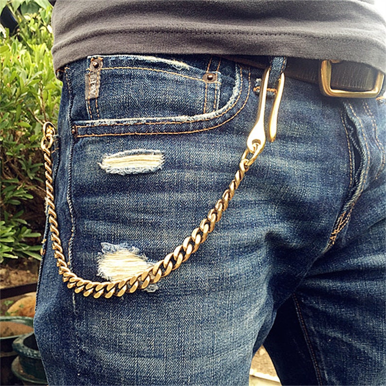 May include: A gold chain with a hook attached to a pair of blue jeans. The chain is worn as a belt loop accessory.