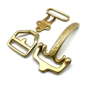 May include: Three gold-toned metal belt buckle pieces. One is a simple rectangular buckle, another is a decorative buckle with an engraved floral design, and the third is a hook and loop closure.