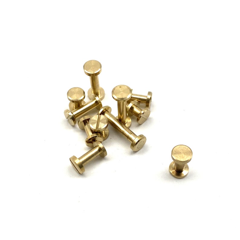 May include: A group of brass screw-in standoffs, also known as spacers, are scattered on a white surface. The standoffs are a shiny gold color and have a round head with a threaded shaft.