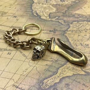 Op de afbeelding: Brass sleutelhanger met een schedelbedel en een haak. De ketting is verbonden met een ring en de haak is aan de ketting bevestigd.