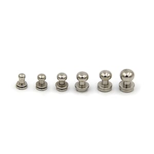 Op de afbeelding: Een set van zes ronde zilveren metalen knoppen in verschillende maten. De knoppen hebben een platte basis met een verhoogde ring rond de rand.