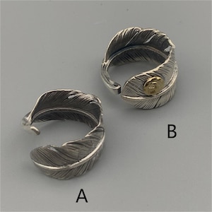 May include: Two silver feather rings. The ring on the left is plain silver. The ring on the right has a gold accent on the feather.