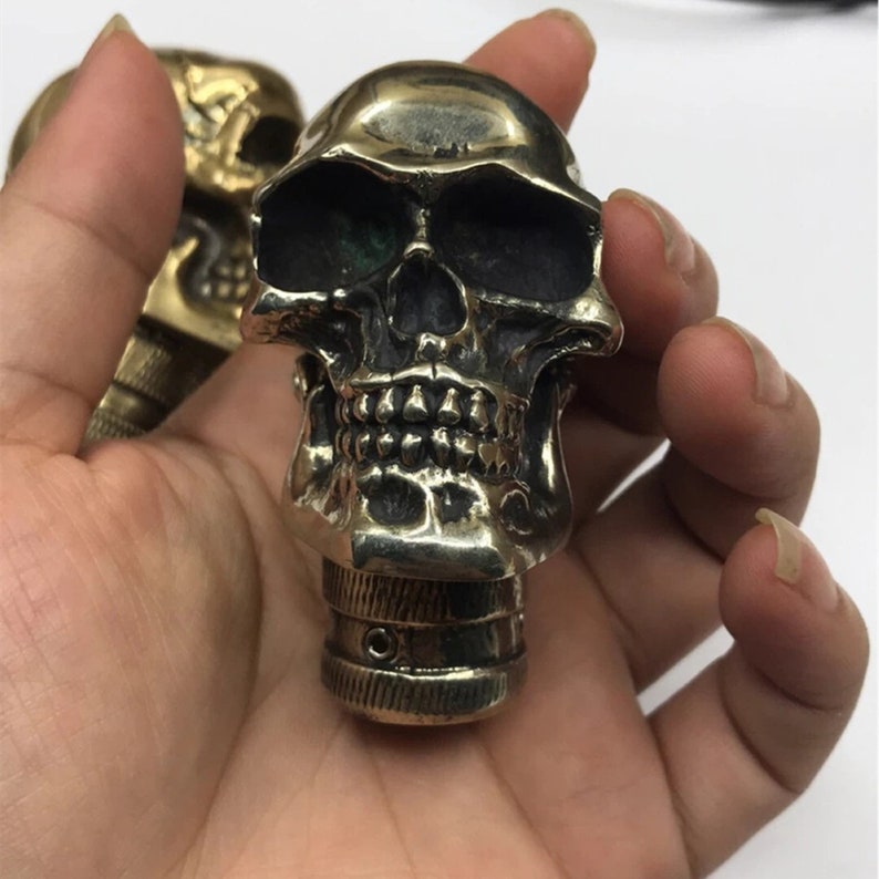 May include: A brass skull-shaped knob with a detailed design. The knob has a threaded base for attaching to a surface.