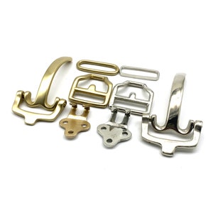 Op de afbeelding: Een set van zeven metalen riemgespen in goud- en zilverkleuren. De gespen zijn in verschillende vormen en maten, waaronder rechthoekig, ovaal en gebogen. Sommige gespen hebben een eenvoudig ontwerp, terwijl andere meer ingewikkelde details hebben.