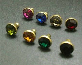 May include: Assortment of eight small, round, gold-toned metal embellishments with colorful glass stones. Each embellishment has a small post on the back.