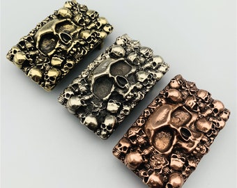 May include: Three belt buckles with a skull design. The buckles are made of metal and have a textured surface. The buckles are in different colors: gold, silver, and copper.