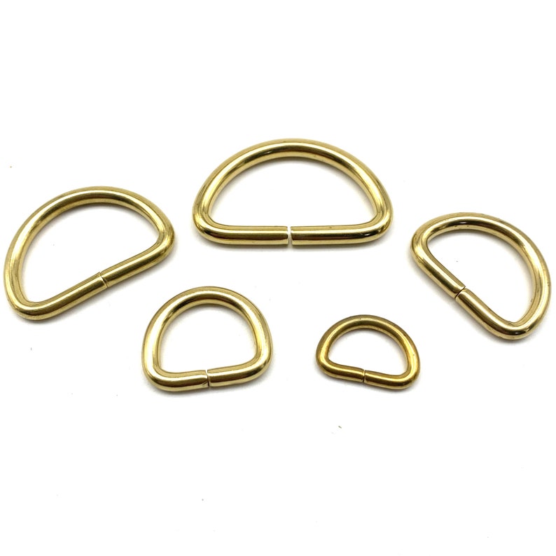 May include: Five gold-colored metal D-rings of varying sizes. The rings are smooth and have a polished finish.