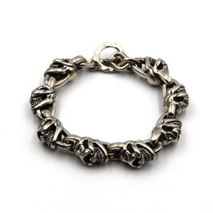 Peut inclure: Un bracelet en argent avec un design de chaîne à maillons orné d'accents en forme de crâne.