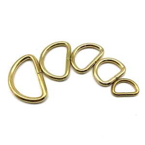 May include: Five gold-colored metal D-rings of varying sizes. The rings are arranged in a semi-circle, with the largest ring at the top and the smallest ring at the bottom.