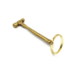 May include: A brass hammer keychain with a round ring. The hammer has a textured surface and a small round head.