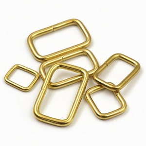 May include: A set of six gold-toned metal D-rings in various sizes. The rings are smooth and have a polished finish.