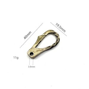 Puede incluir: Un mosquetón de metal dorado con un diseño retorcido. Mide 4,95 cm de largo, 4 cm de ancho y 0,39 cm de grosor. Pesa 11 gramos.