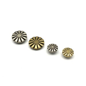 May include: Four decorative metal buttons in different sizes. The buttons are round and have a sunburst design. The buttons are silver and gold.