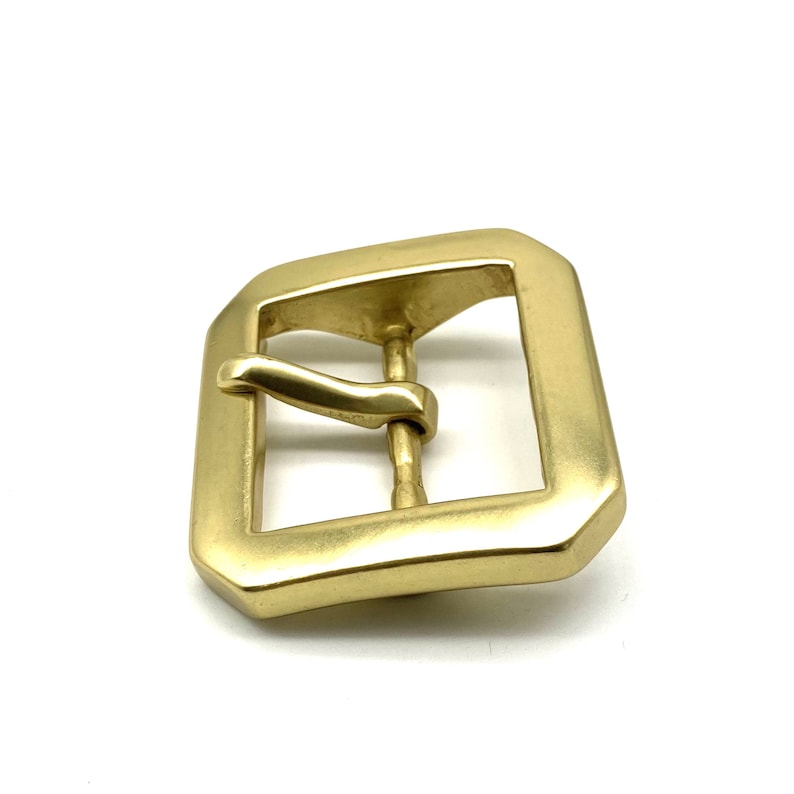 May include: A gold-toned metal buckle with a rectangular shape and a smooth, polished finish. The buckle has a single prong and a curved tongue.