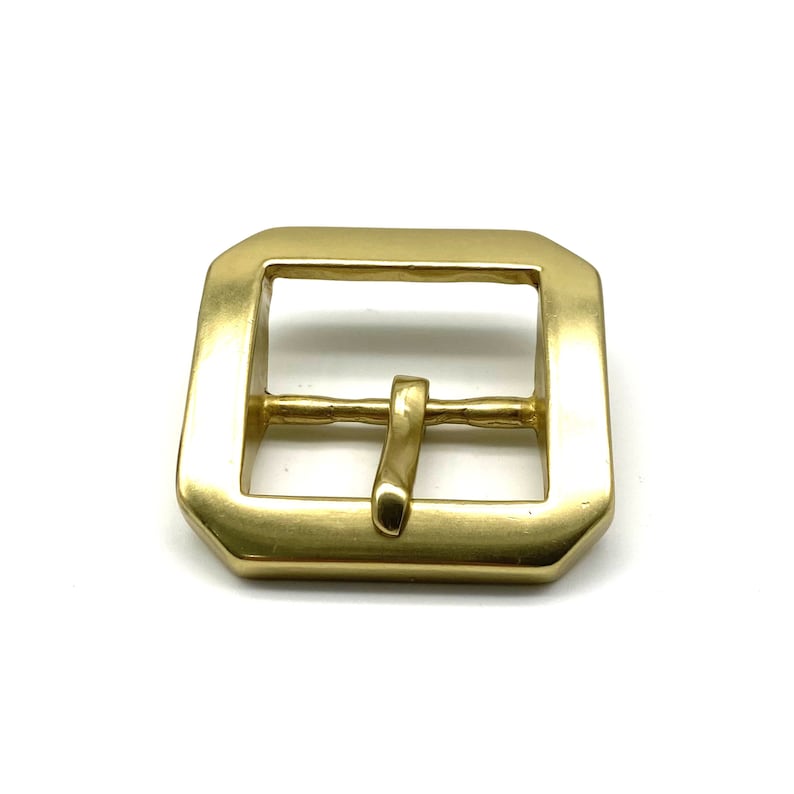 May include: A gold-toned metal buckle with a rectangular shape and a smooth finish. The buckle has a single prong for attaching to a strap.